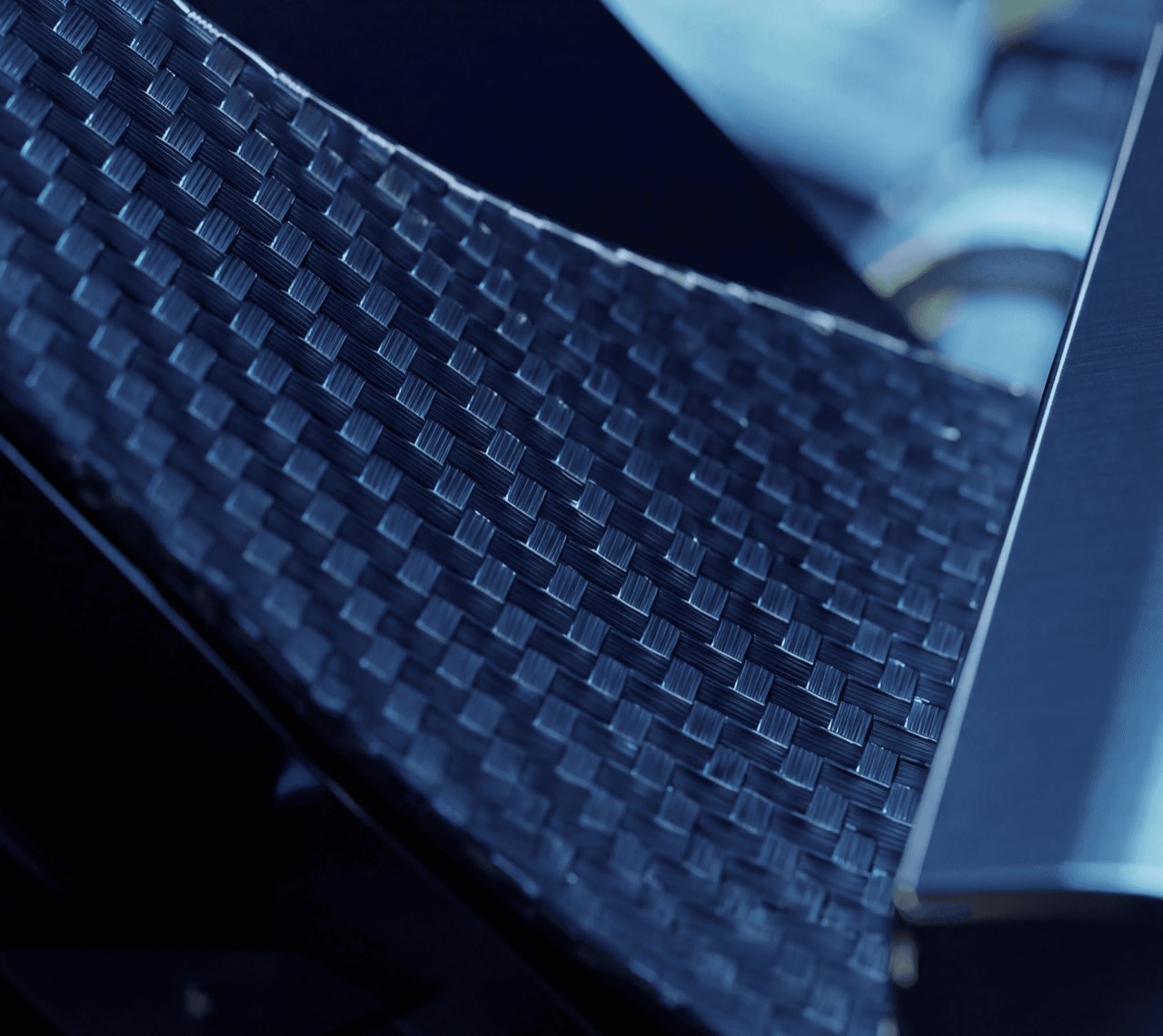 Macro view of the woven carbon-fibre Carbitex sheet, curving as it flexes under cool blue light.